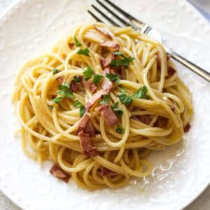 Close-up of spaghetti carbonara with pancetta and parsley on a white plate.