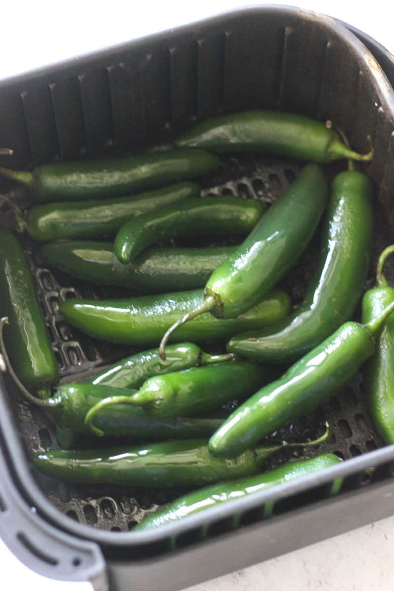 Green jalapeño peppers in a black basket, ready for culinary use.