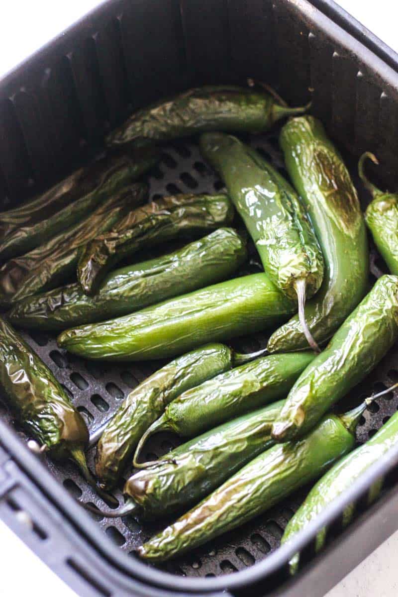 Fresh roasted green chilies in a black basket for culinary use.