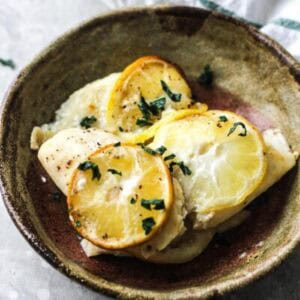 Delicious baked fish with lemon slices and herbs in a rustic bowl.