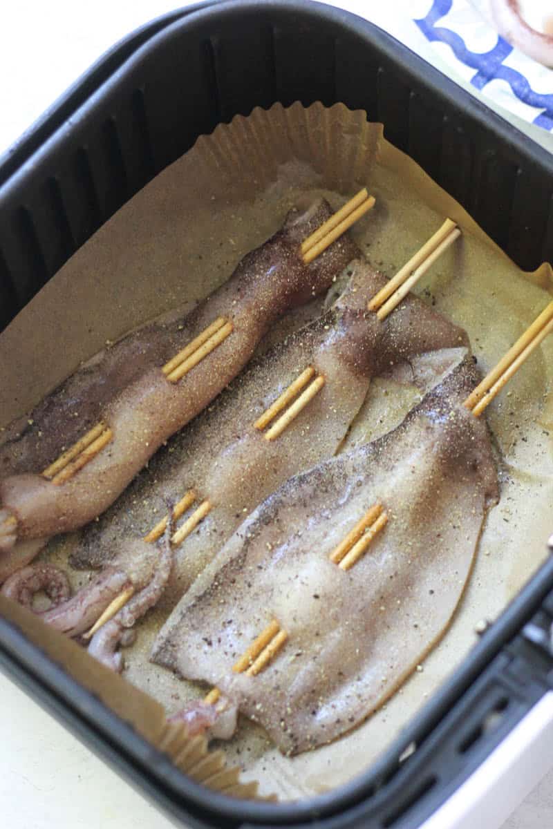 Raw squid skewers seasoned and ready for grilling in a black basket.