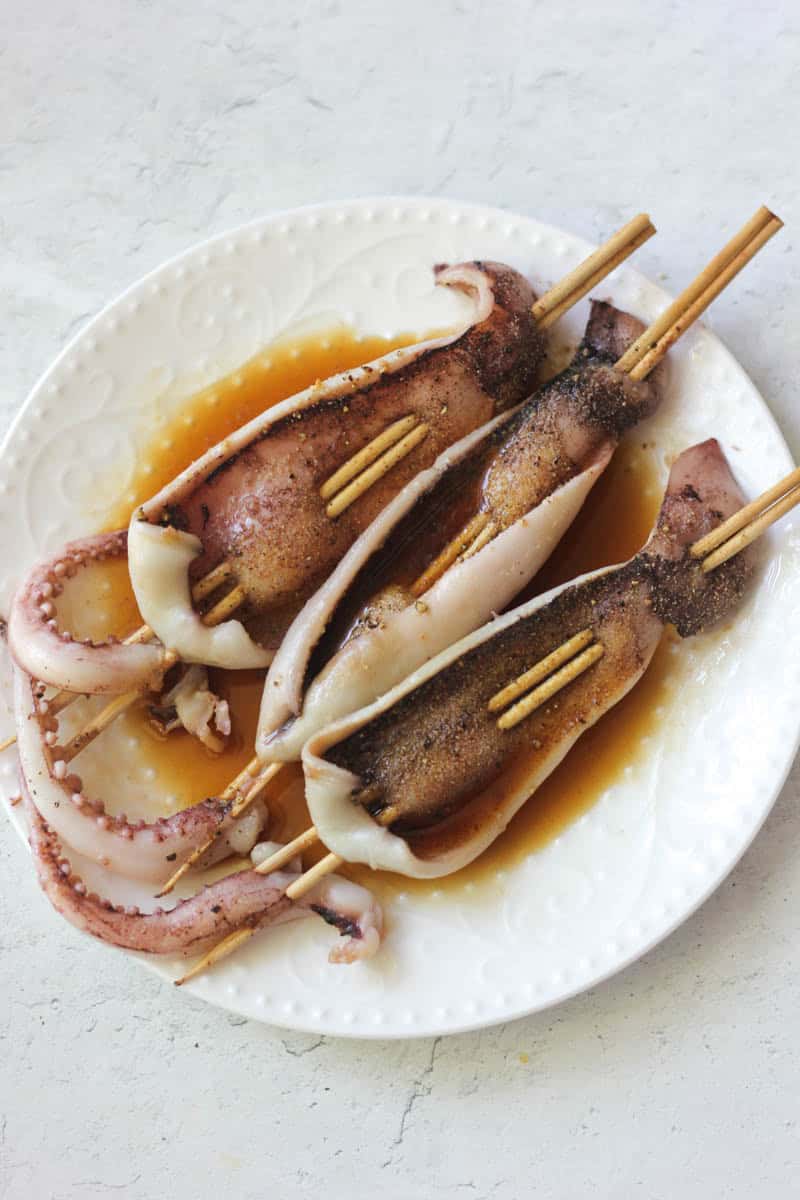 Delicious grilled squid skewers served with savory sauce on a white plate.