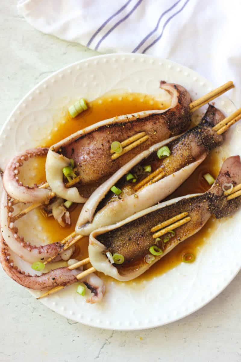 Delicious grilled squid skewers garnished with green onions and served with savory sauce.