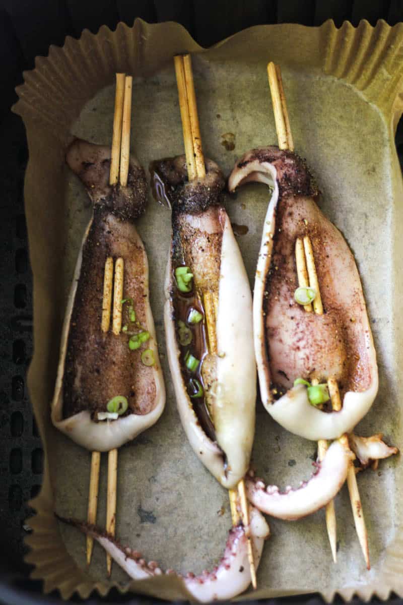 Fresh grilled squid skewers garnished with green onions on a baking sheet.
