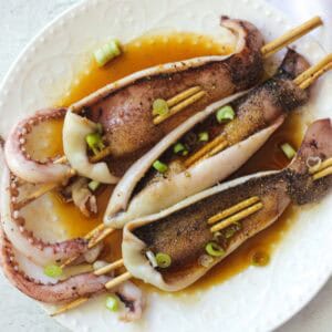 Delicious grilled squid skewers garnished with green onions on a white plate.