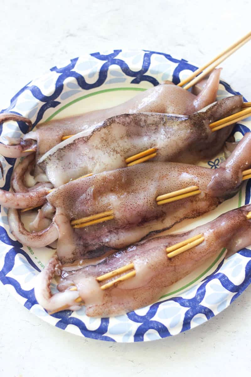 Fresh grilled squid skewers served on a decorative plate with skewers for easy eating.