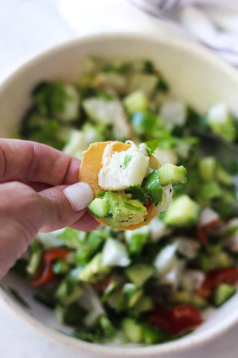Close-up of a hand holding a piece of cucumber and tomato salad.