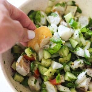 Hand adding a cracker to a bowl of chicken salad with cucumbers and tomatoes.