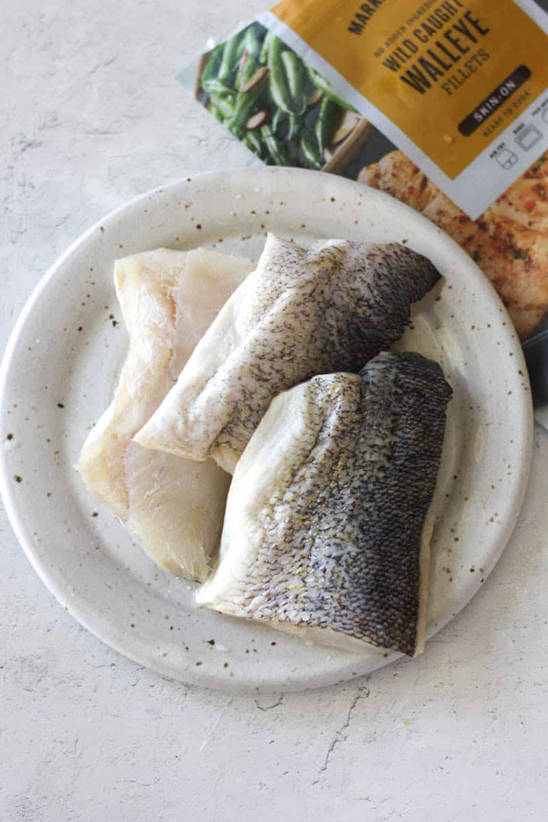 Raw fish fillets on a white plate, ready for cooking or grilling.
