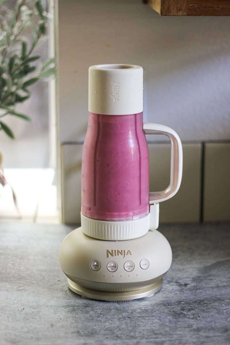 Ninja blender blending a pink smoothie on a kitchen counter.