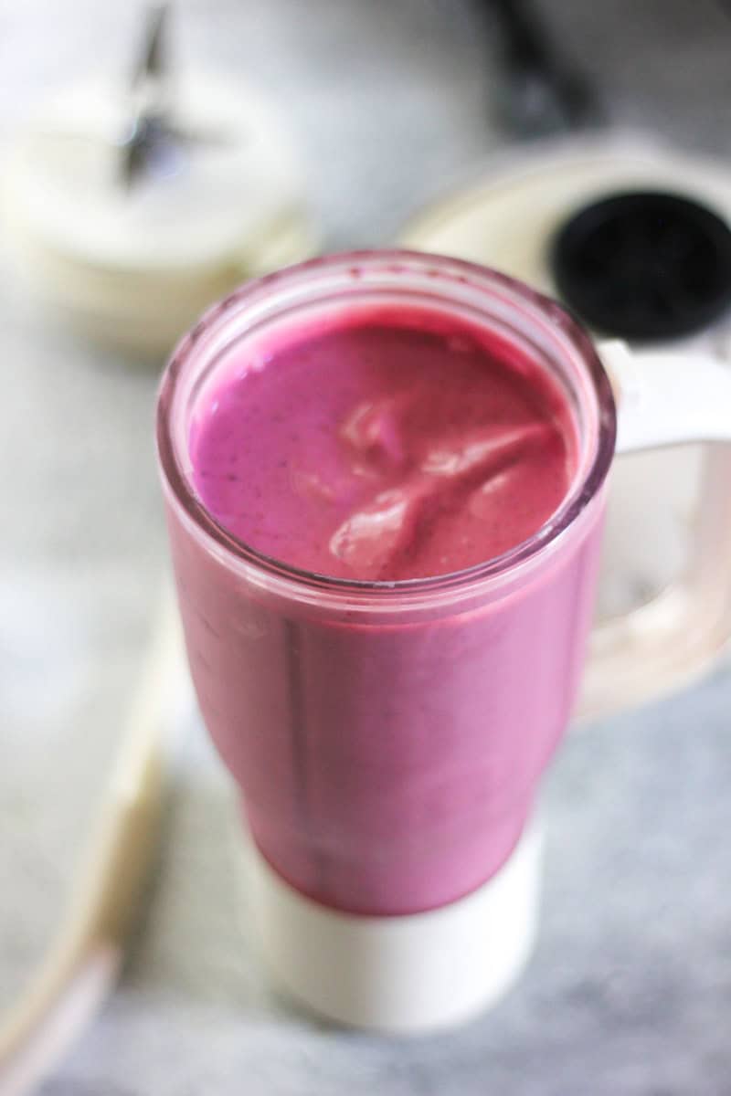Vibrant pink berry smoothie in a glass blender cup for a nutritious snack.