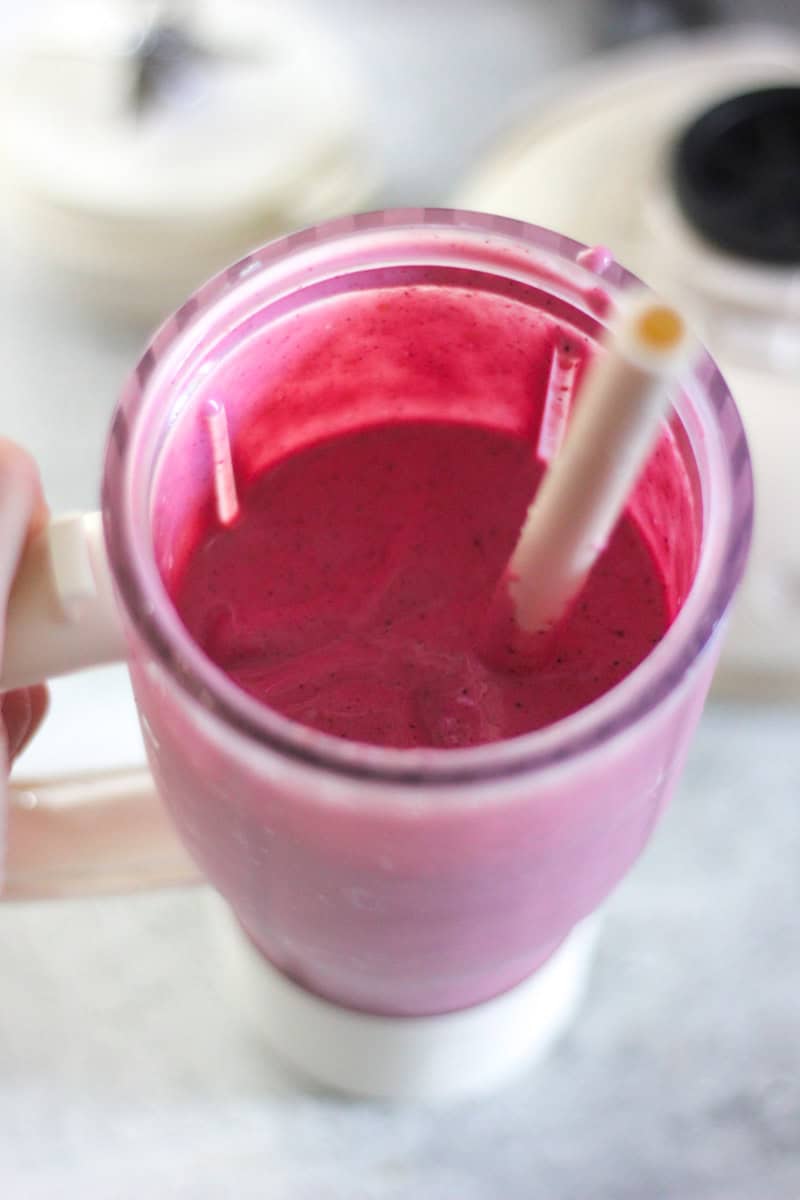 Close-up of a pink berry smoothie in a blender with a straw.