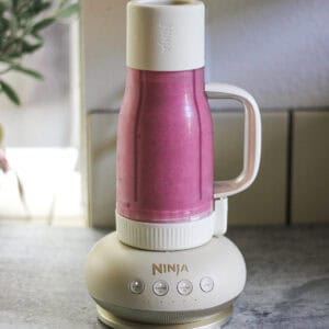 Ninja blender blending a pink smoothie on a kitchen countertop.