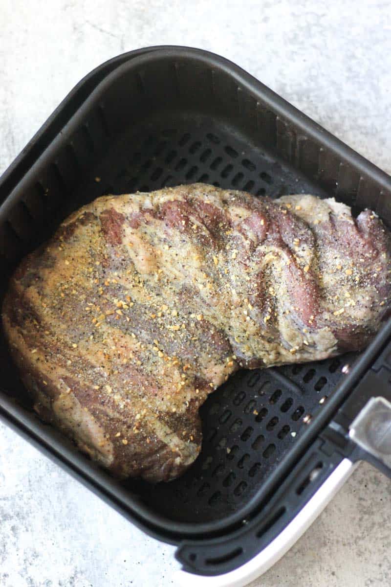 Beef roast seasoned with spices in an air fryer basket.