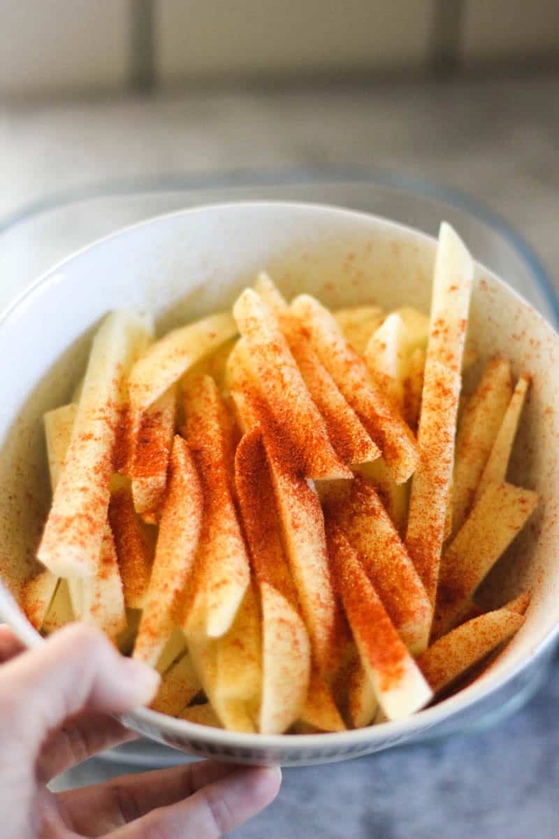 Fries slices in a bowl with paprika seasoning.