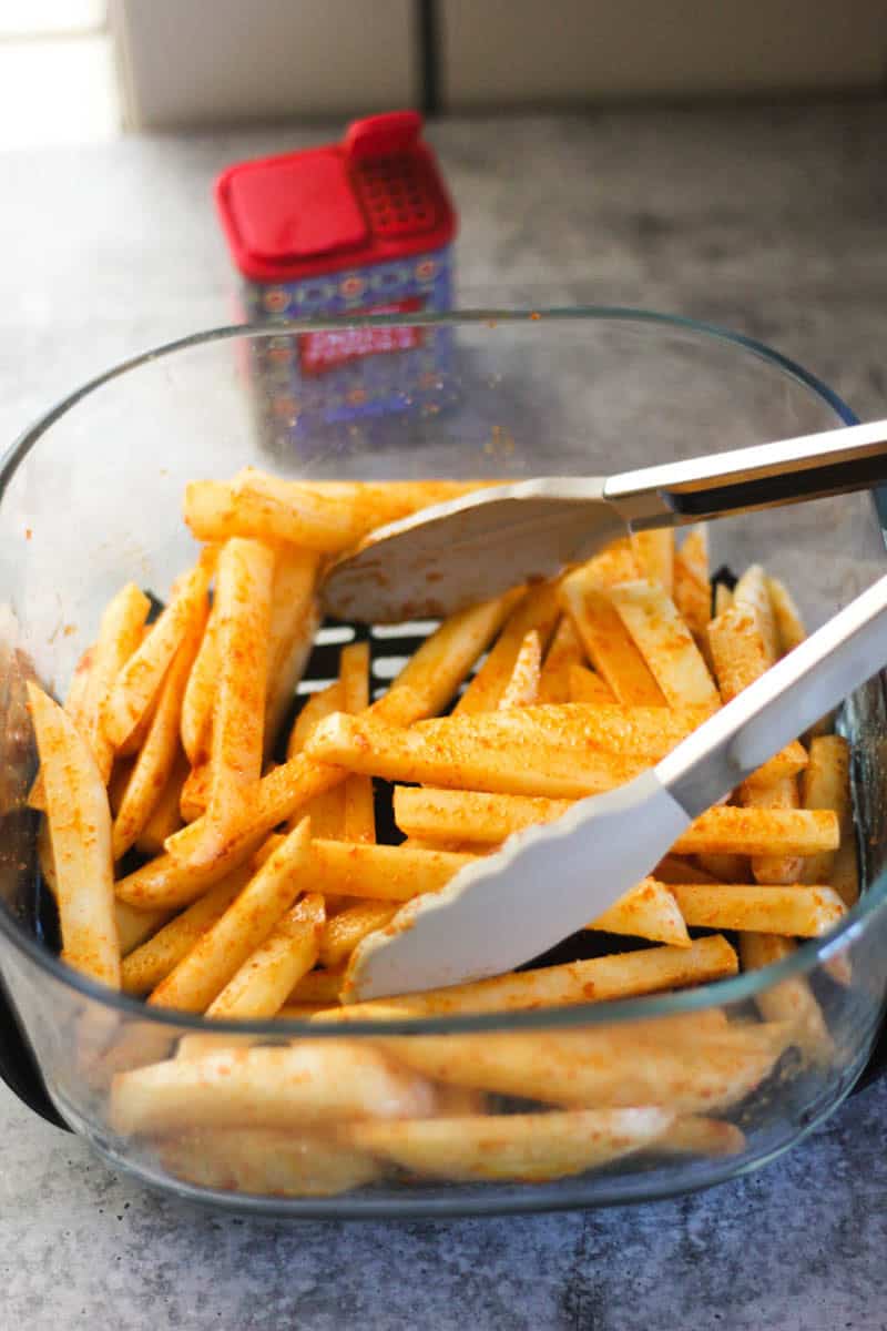 Golden crispy french fries in a glass baking dish with tongs.