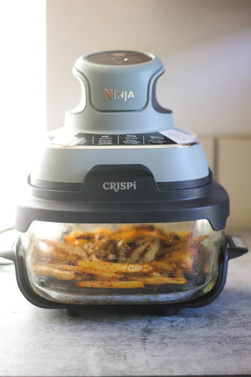 Ninja CRISPi air fryer on kitchen counter with fries inside and soft lighting.