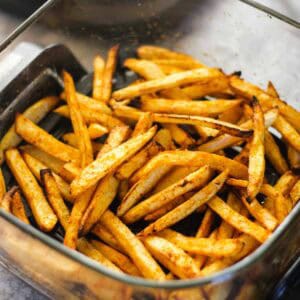 Crispy seasoned French fries in a glass bowl.