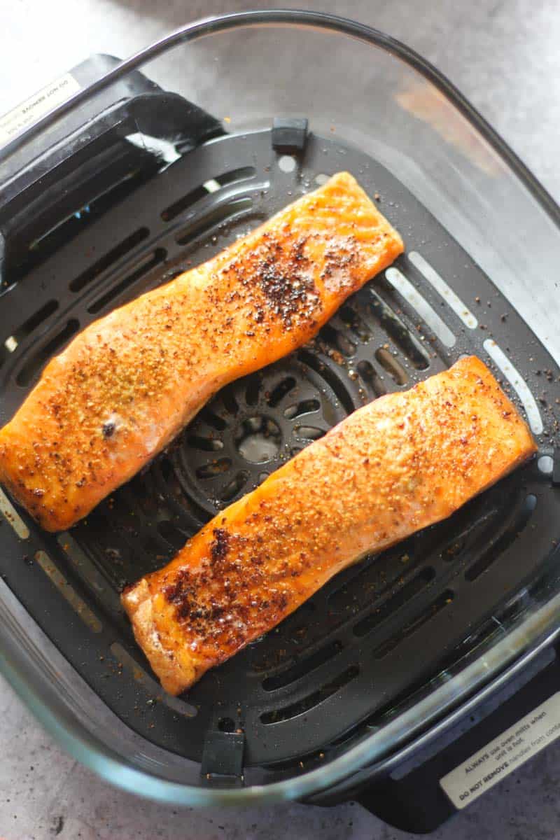Two seasoned salmon fillets cooking in an air fryer basket.