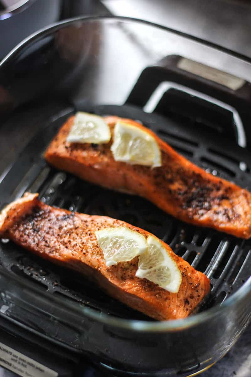 Grilled salmon fillets with lemon wedges in a pan.
