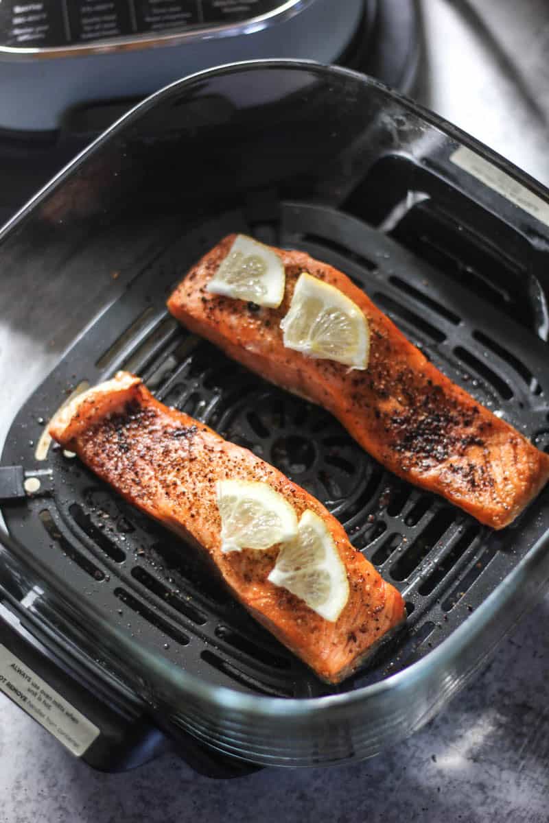 Salmon fillets cooking in air fryer with lemon wedges on top.