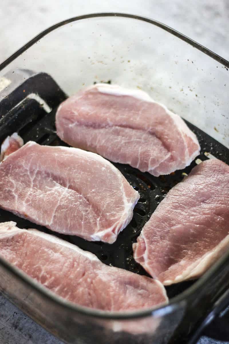Juicy pork chops cooking in a glass baking dish on a grill pan.