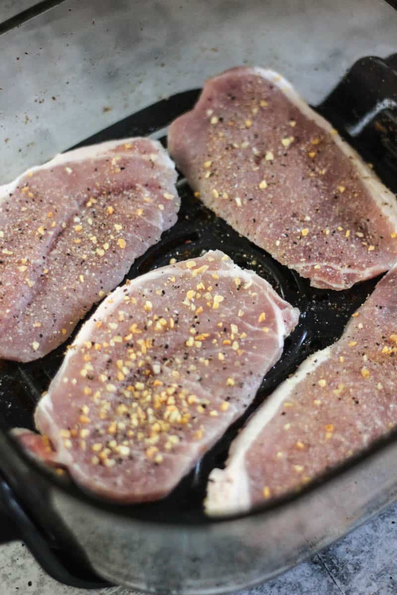 Three seasoned pork chops in a skillet ready to cook.