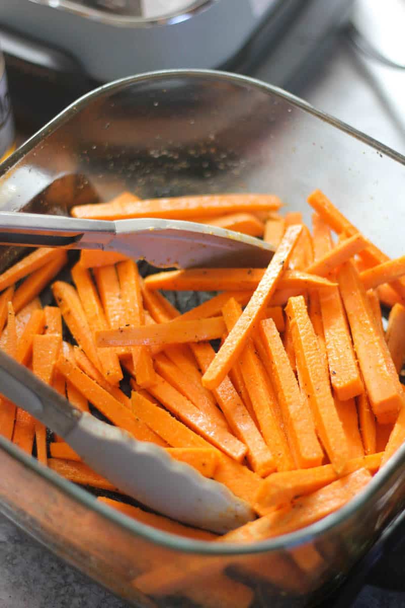 Shredded carrots in a glass bowl with tongs, vibrant orange color.