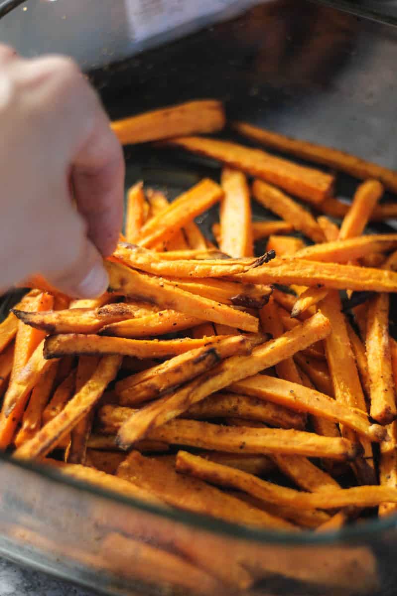 Golden crispy french fries being sprinkled with spices.